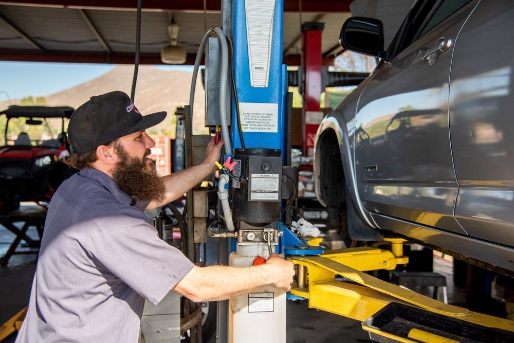 Mechanic using a lift to work on a silver car in an auto repair shop