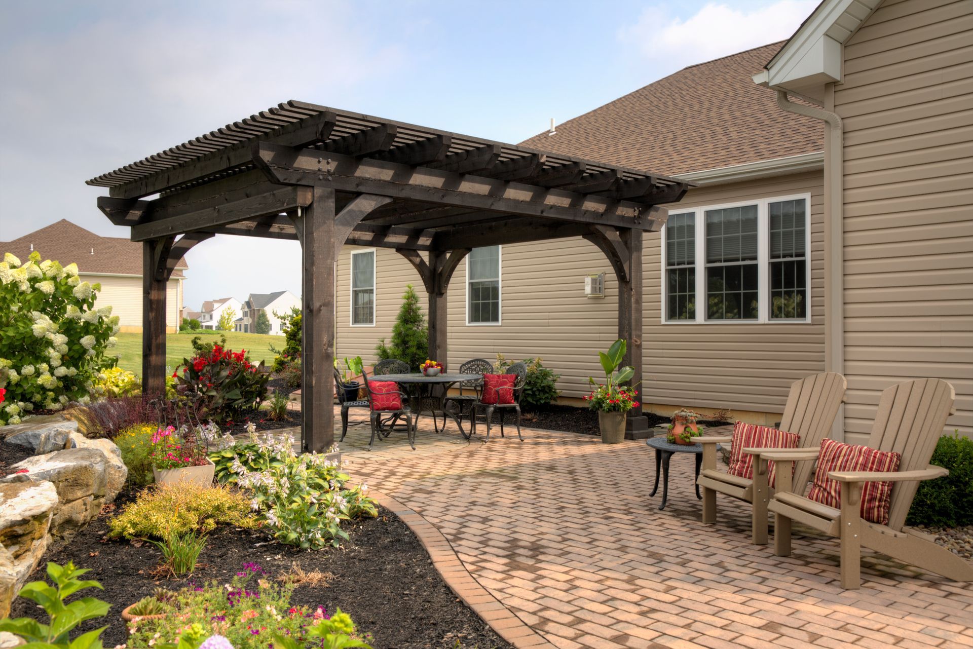 A patio with a pergola and chairs in front of a house.