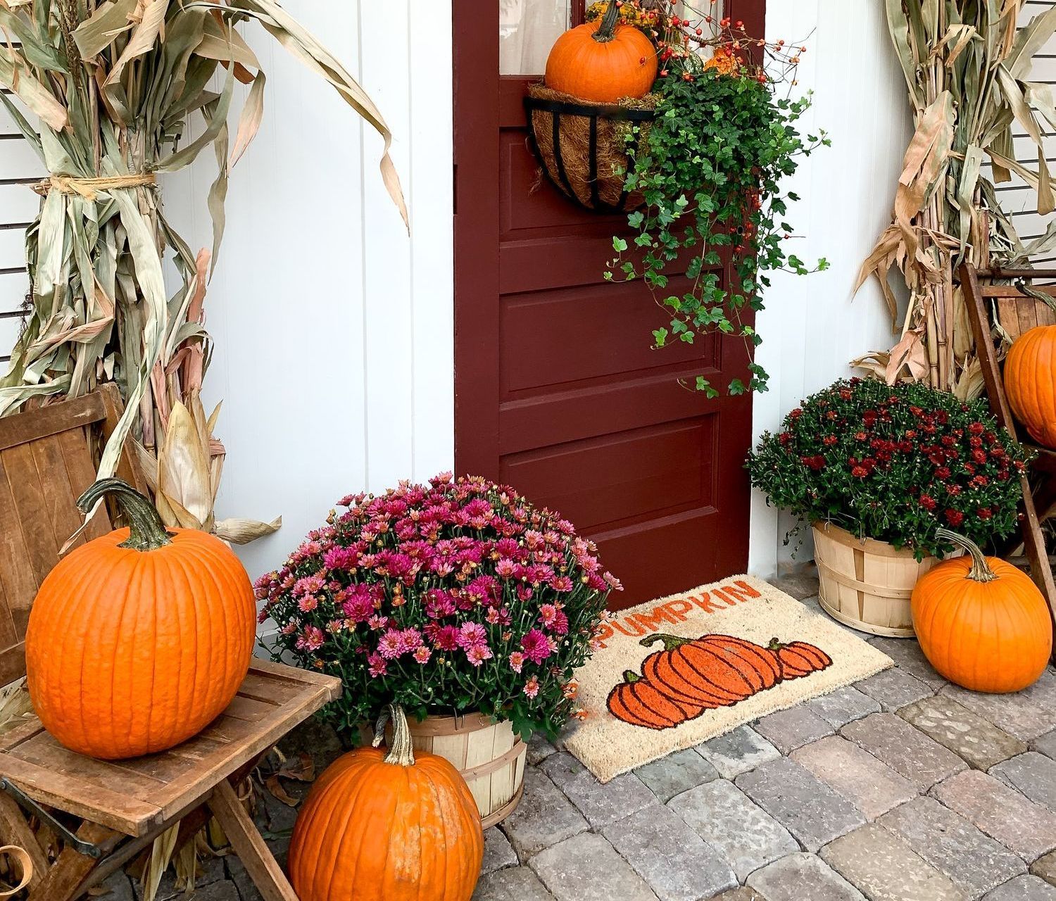 Fall porch decorated with pumpkins, mums, and corn stalks.