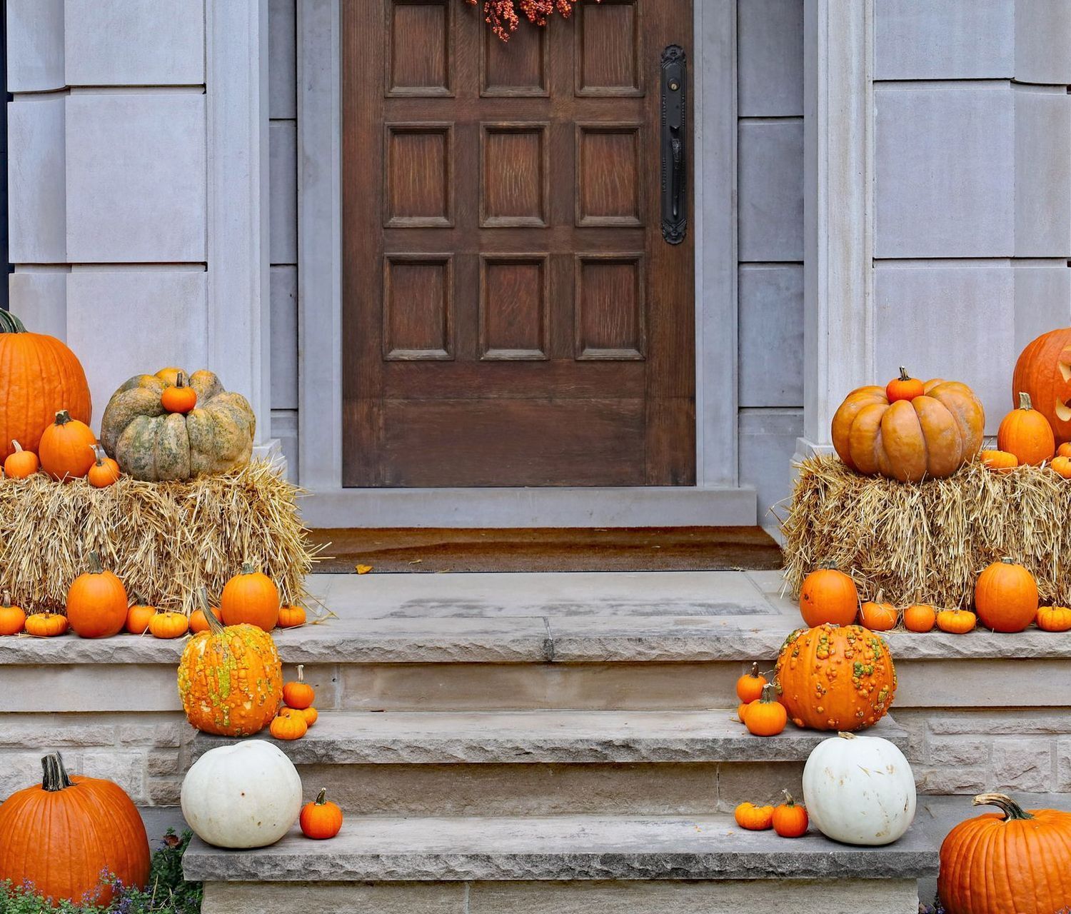 A doorway decorated with pumpkins on hay bales and steps for fall.