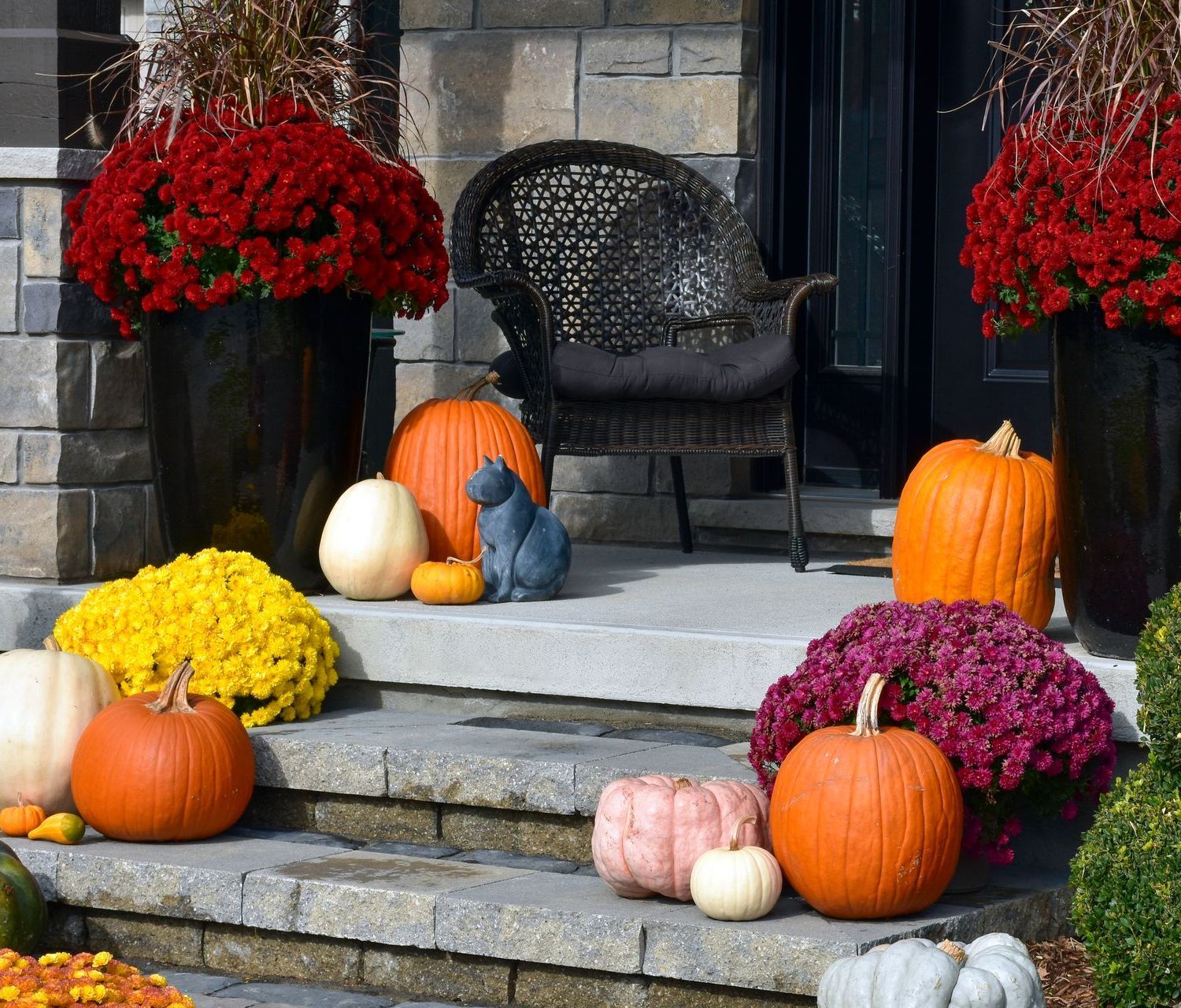Fall porch decorated with pumpkins, mums, and a wicker chair.