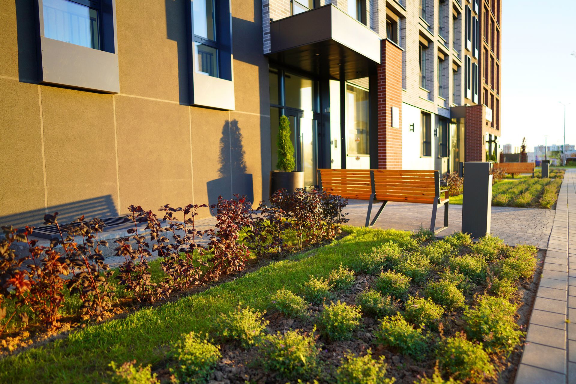 Modern building exterior with landscaped flower beds, bench, and entrance under a canopy.