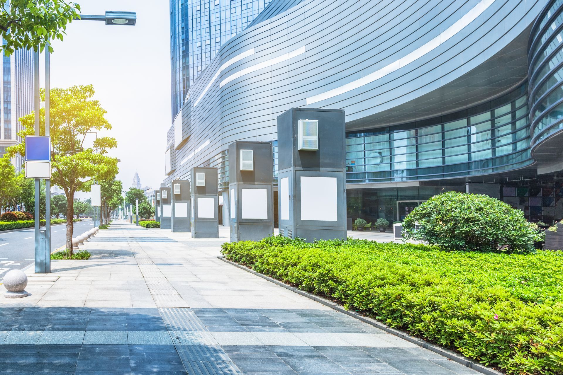 Modern glass office building with curved facade, sidewalk, trees, and bright green landscaping