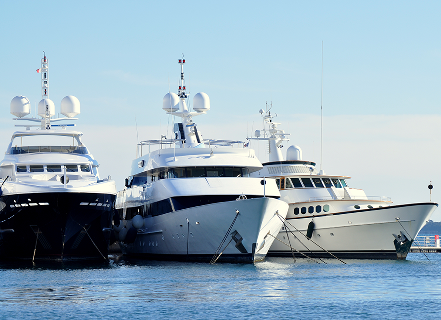 Three luxury yachts docked side by side on calm blue water under a clear sky