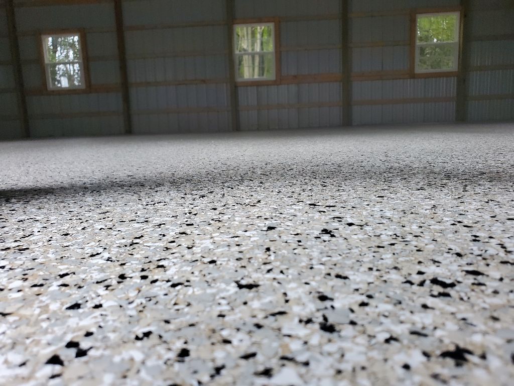Epoxy-coated concrete floor with speckled light and dark gray flakes in a large metal building.