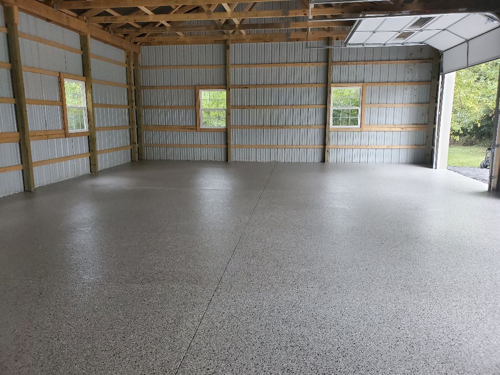 Interior of a large, empty garage with a polished concrete floor, windows, and an open garage door.