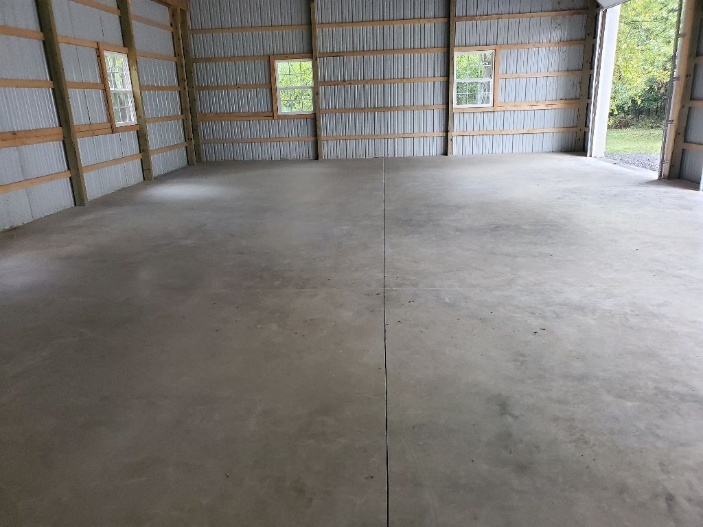 Interior of a large empty garage with a concrete floor, three windows, and metal siding.