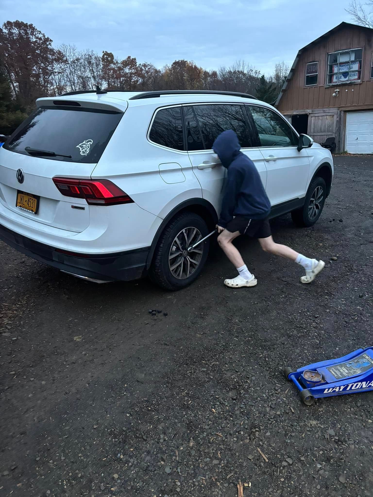 A man is pushing a white suv in a parking lot.