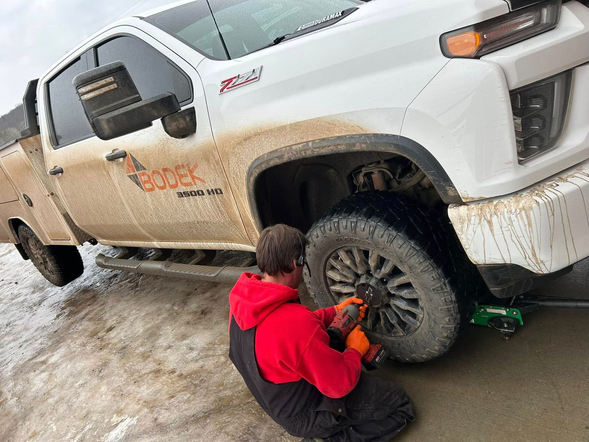 A man is changing a tire on a white truck.