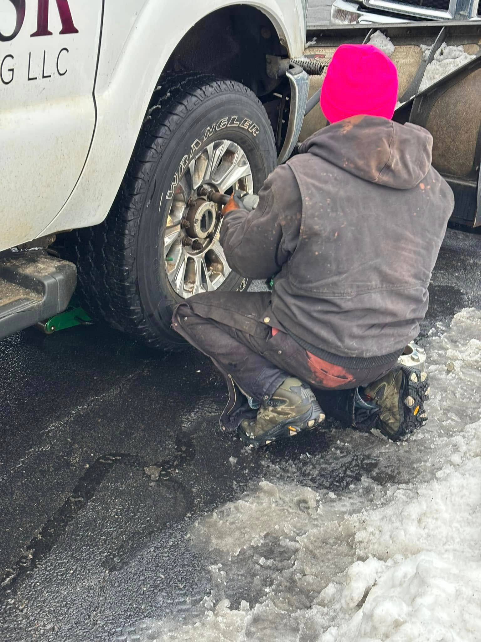 A man in a pink hat is kneeling down to change a tire on a truck.