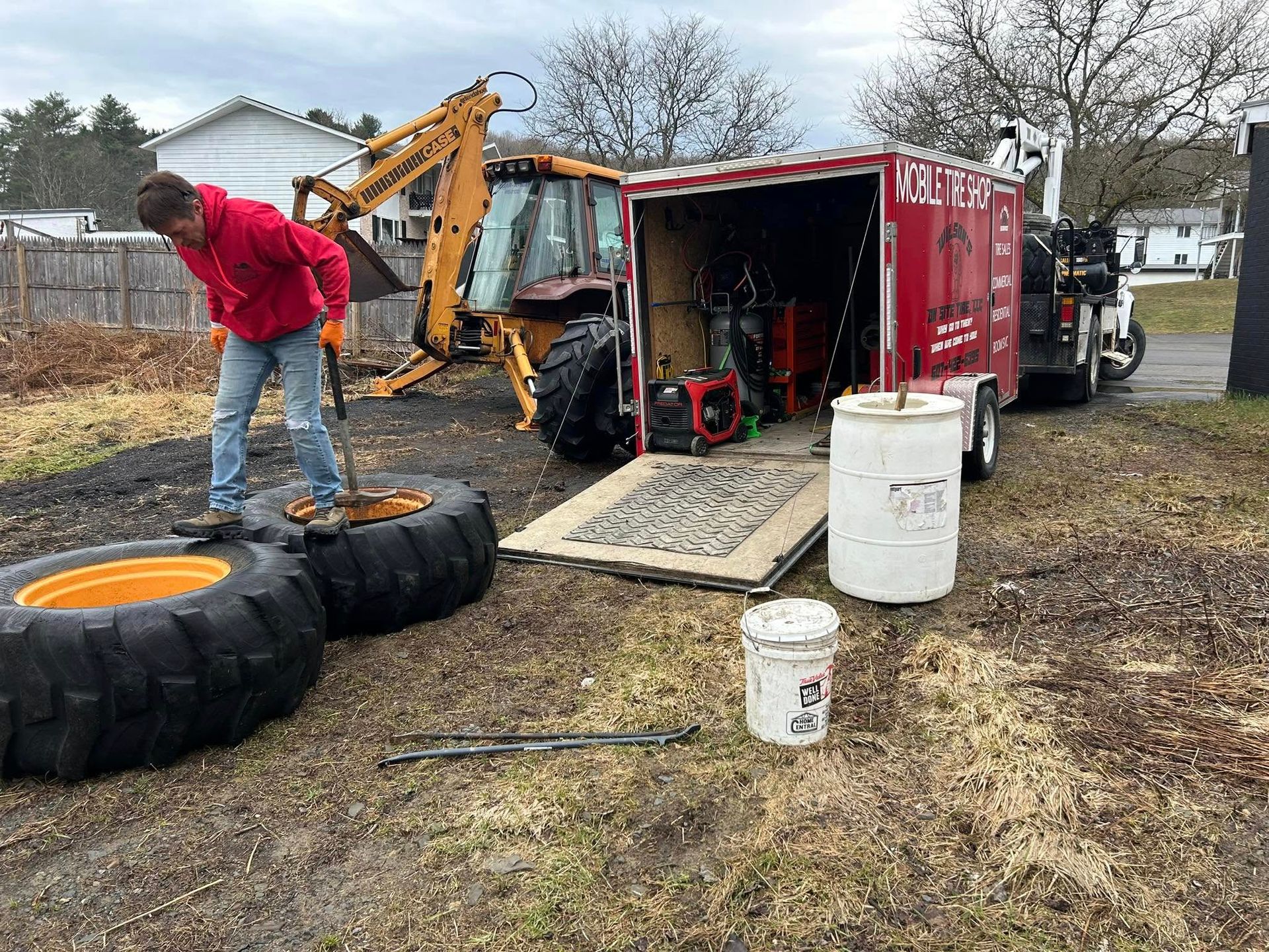 A man is changing a tire on a tractor in front of a trailer.