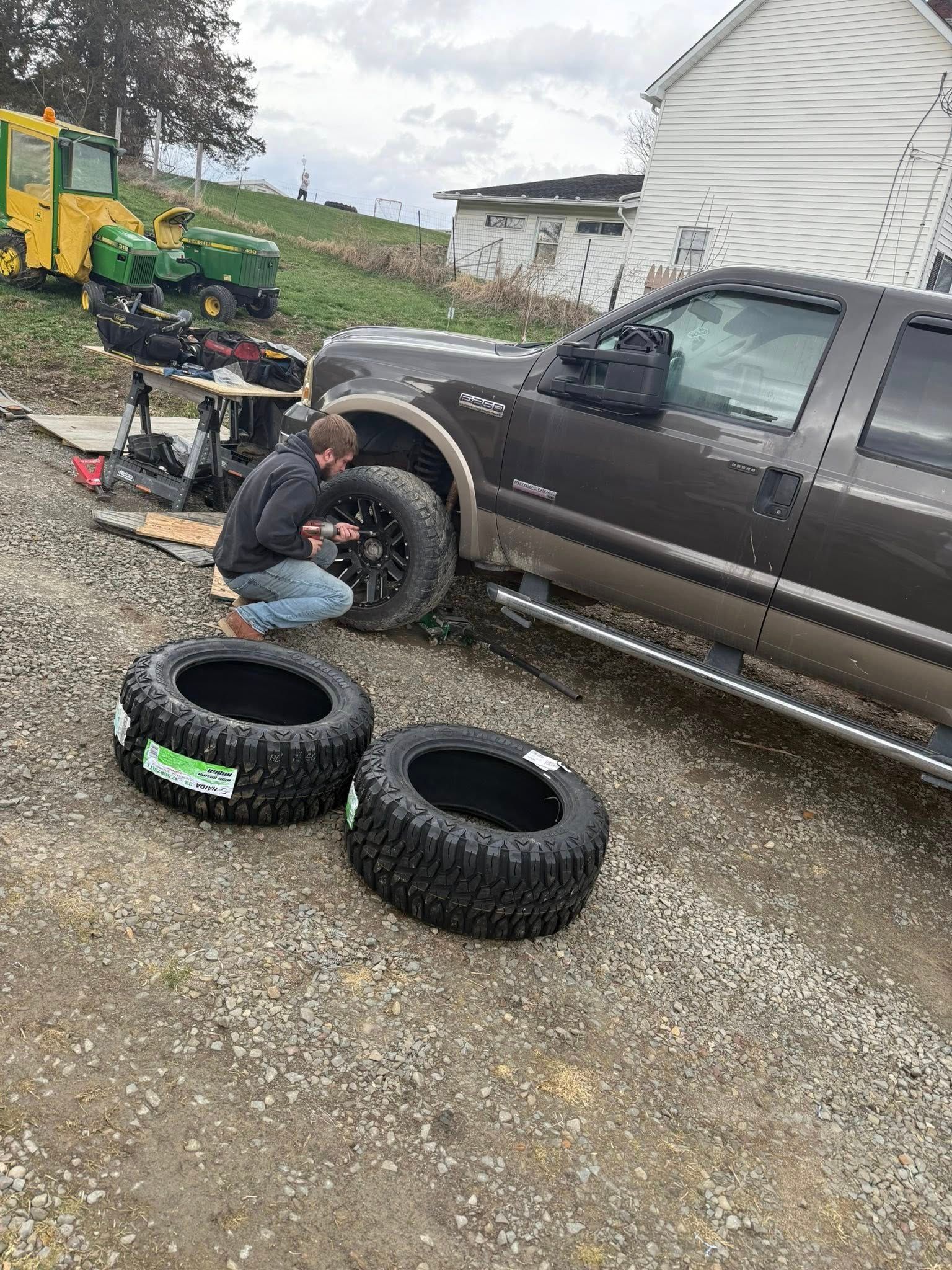 A man is changing tires on a truck in a gravel lot.