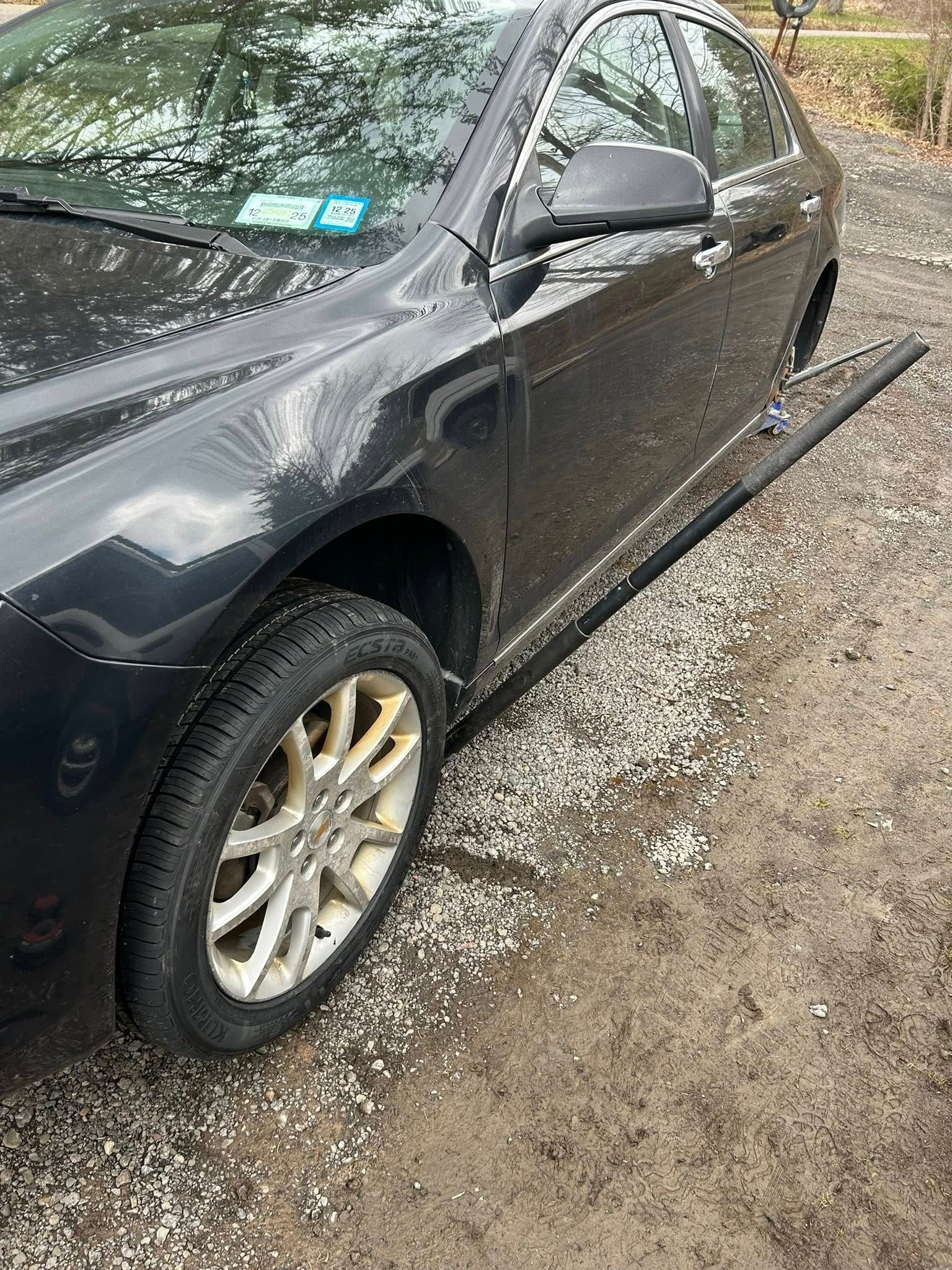 A black car is parked on gravel in a parking lot.