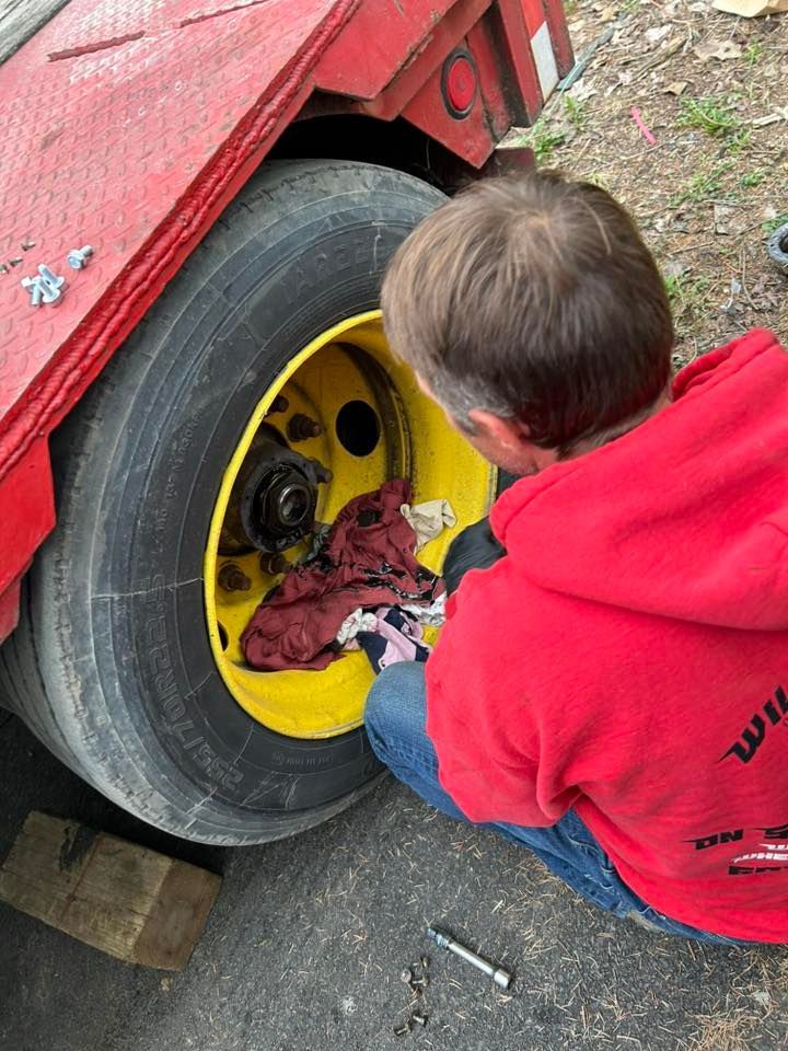 A young boy in a red hoodie is working on a truck tire.