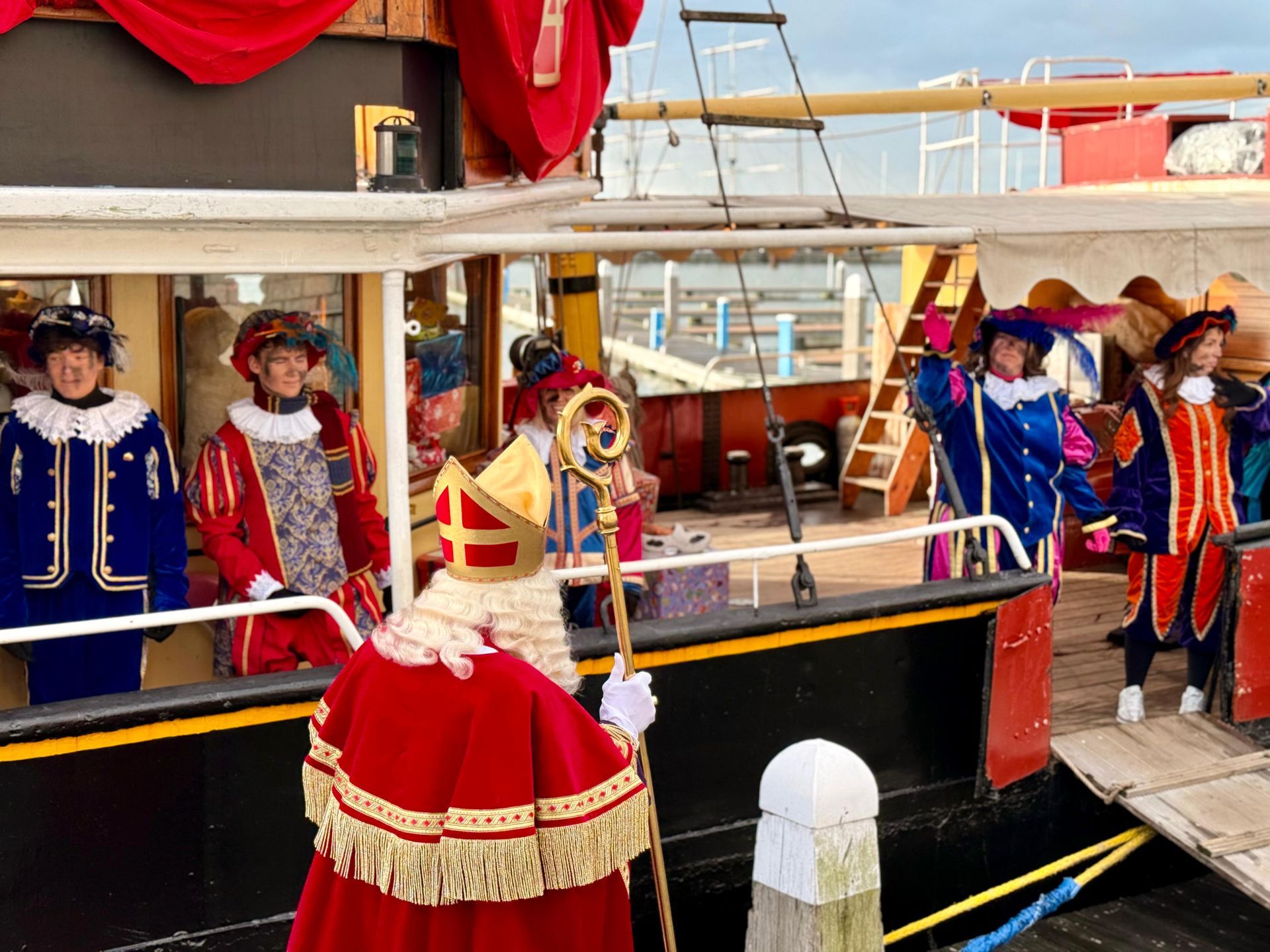 Sinterklaas en zijn helpers in traditionele kleding aan boord van een boot in een haven.