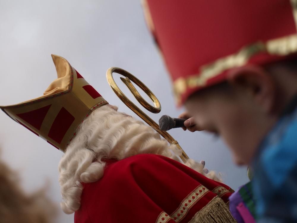 Een persoon verkleed als Sinterklaas, met mijter en gouden staf in de hand, met een wazige voorgrond.