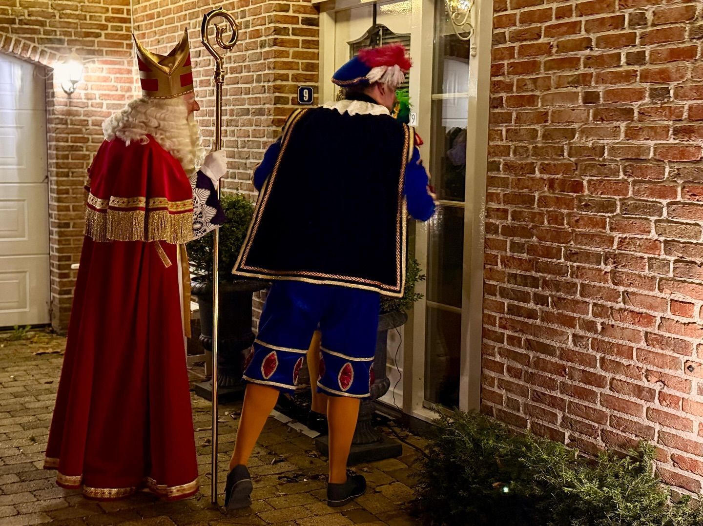 Twee verklede personen staan ​​'s nachts bij een bakstenen muur in een warm verlicht steegje.