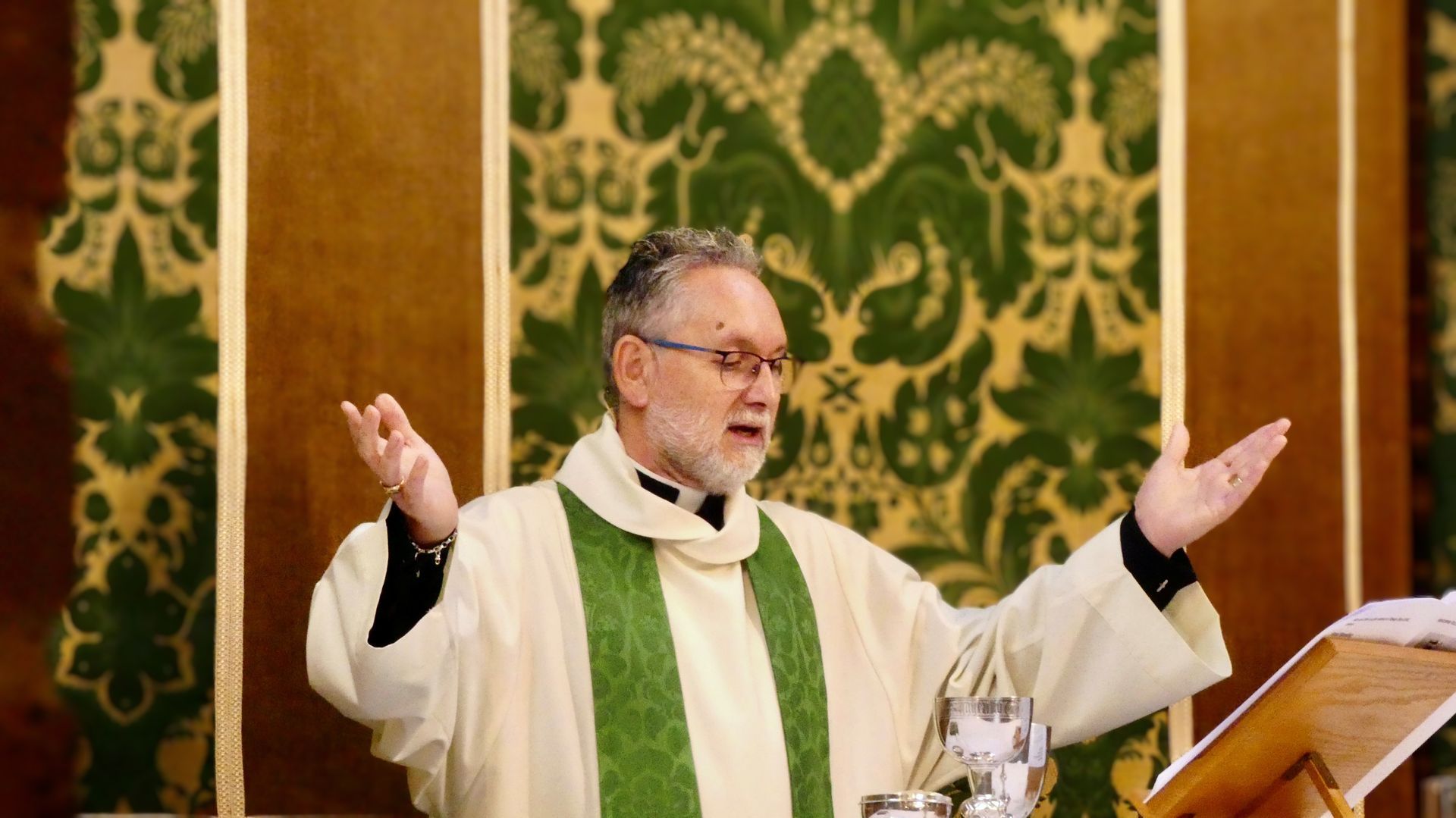 St Augustine Church Priest in green vestments preaching with raised arms at a church altar
