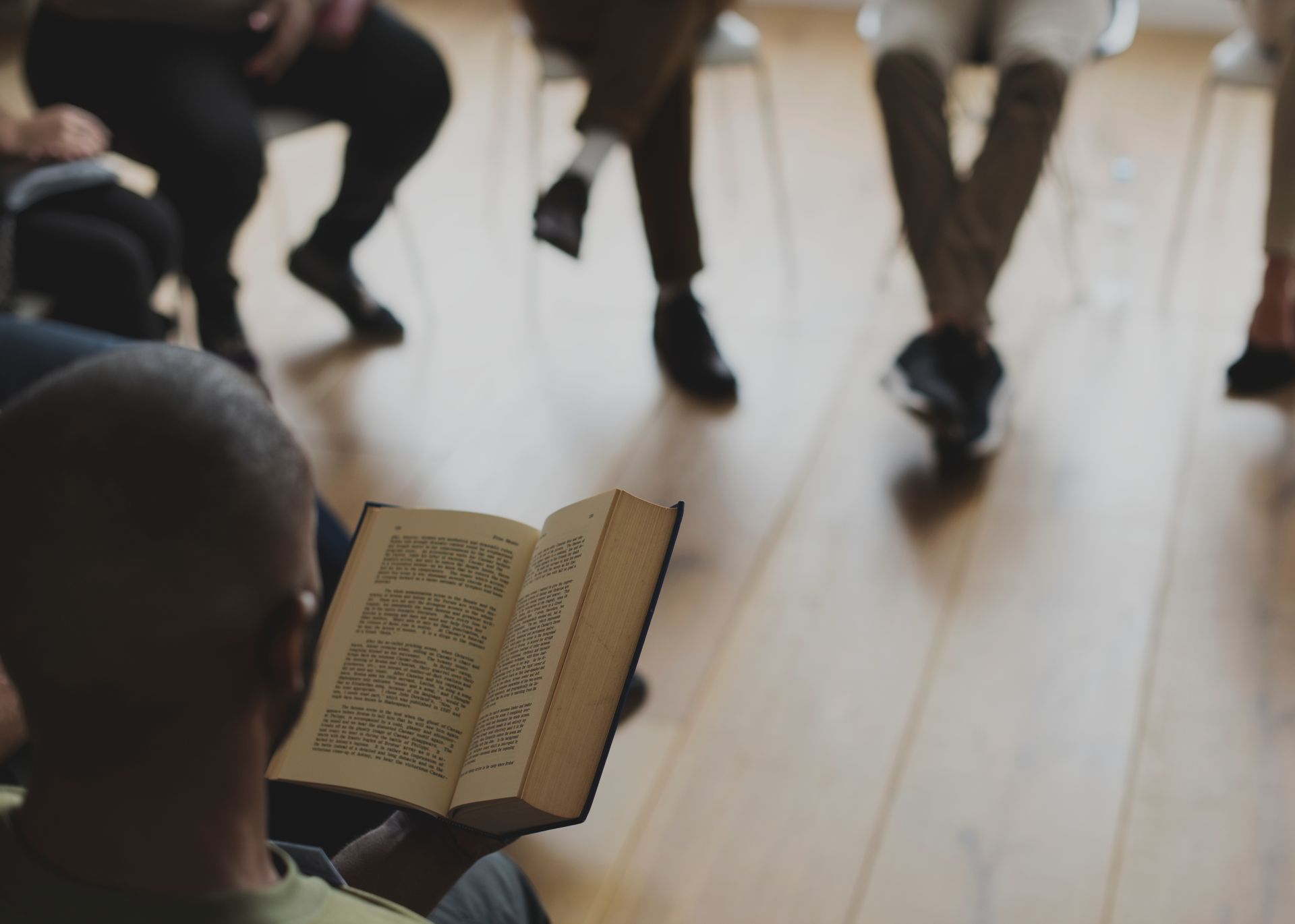 Person reading an open book in a meeting circle on a wooden floor