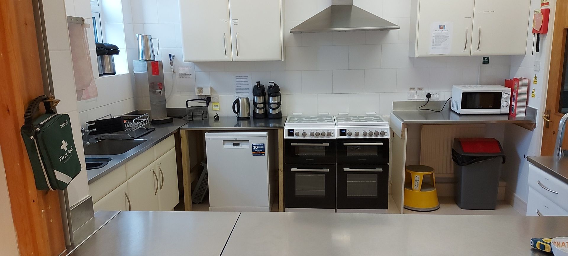 St Augustine Church Barnard Room Hire - Small kitchen with white cabinets, stove, fridge, sink, and countertop appliances.