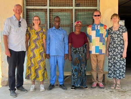 Six people standing in a row outside a building, posing for a group photo.