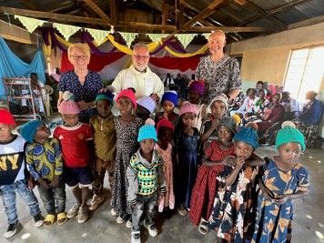 Group of children posing with adults under a decorated tent, wearing colorful clothes and hats.
