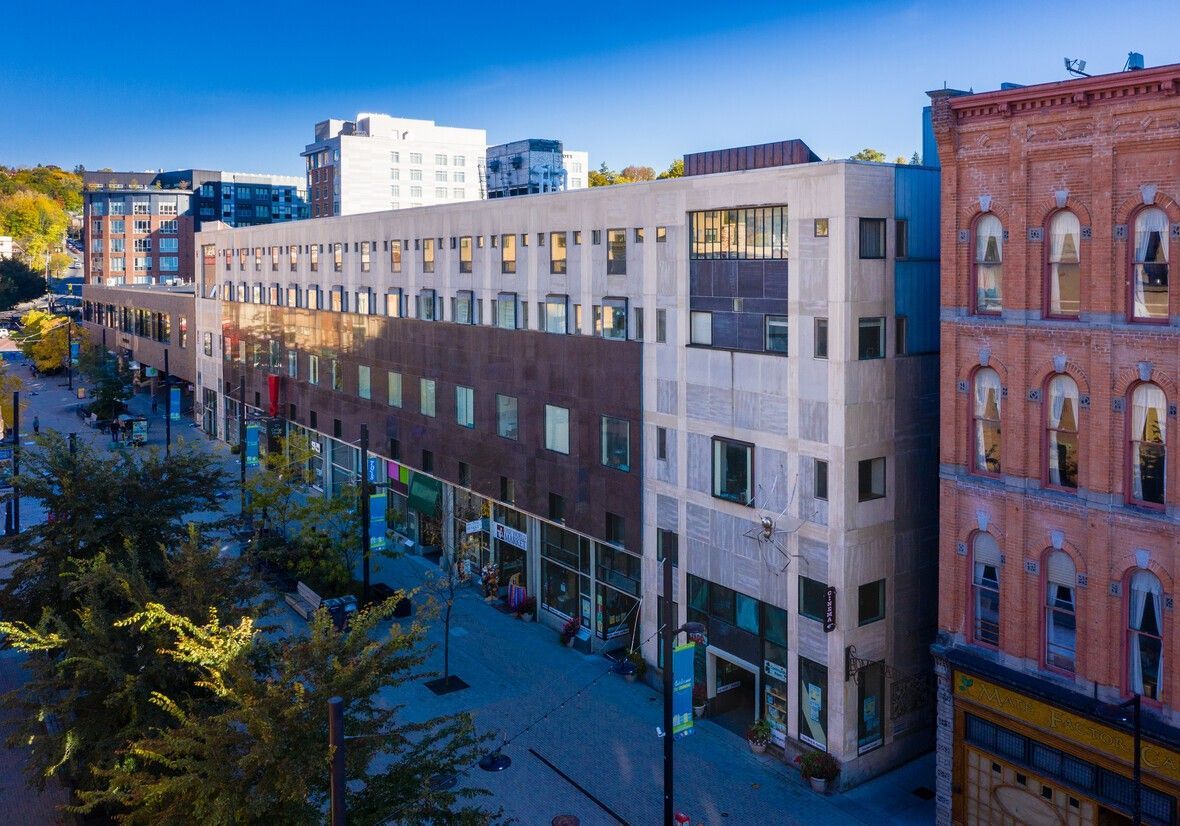 Multi-story building with storefronts and patterned facade, on a brick-paved street with trees.
