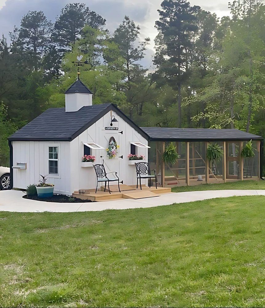 Small white cottage with dark roof and porch in a grassy yard, surrounded by trees.