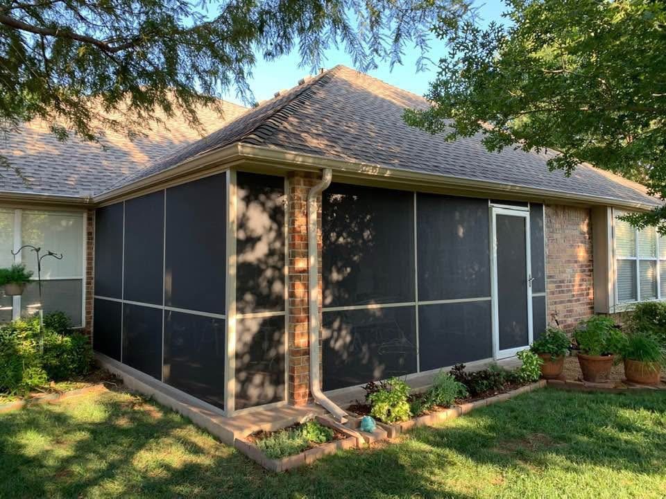 Screened patio extension with dark mesh panels beside a brick house and potted plants