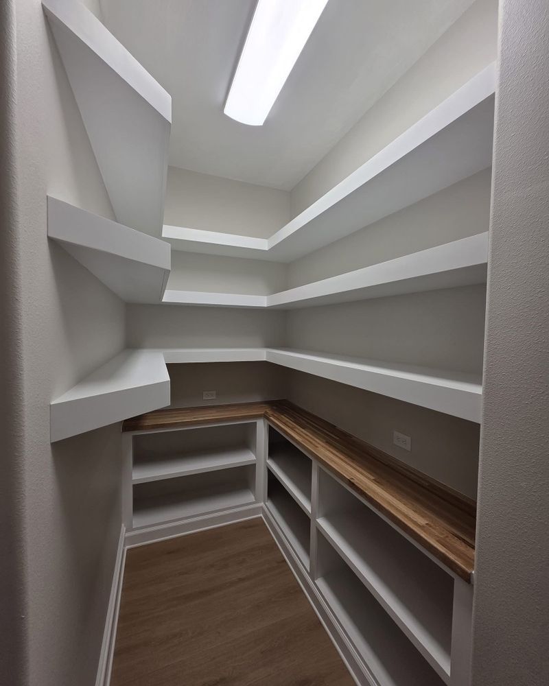 Empty walk-in closet with white shelves, wood countertops, and a skylight overhead