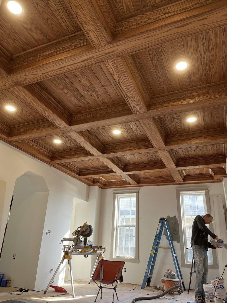 Worker installing lighting in a room with a decorative wood-paneled ceiling and ladder