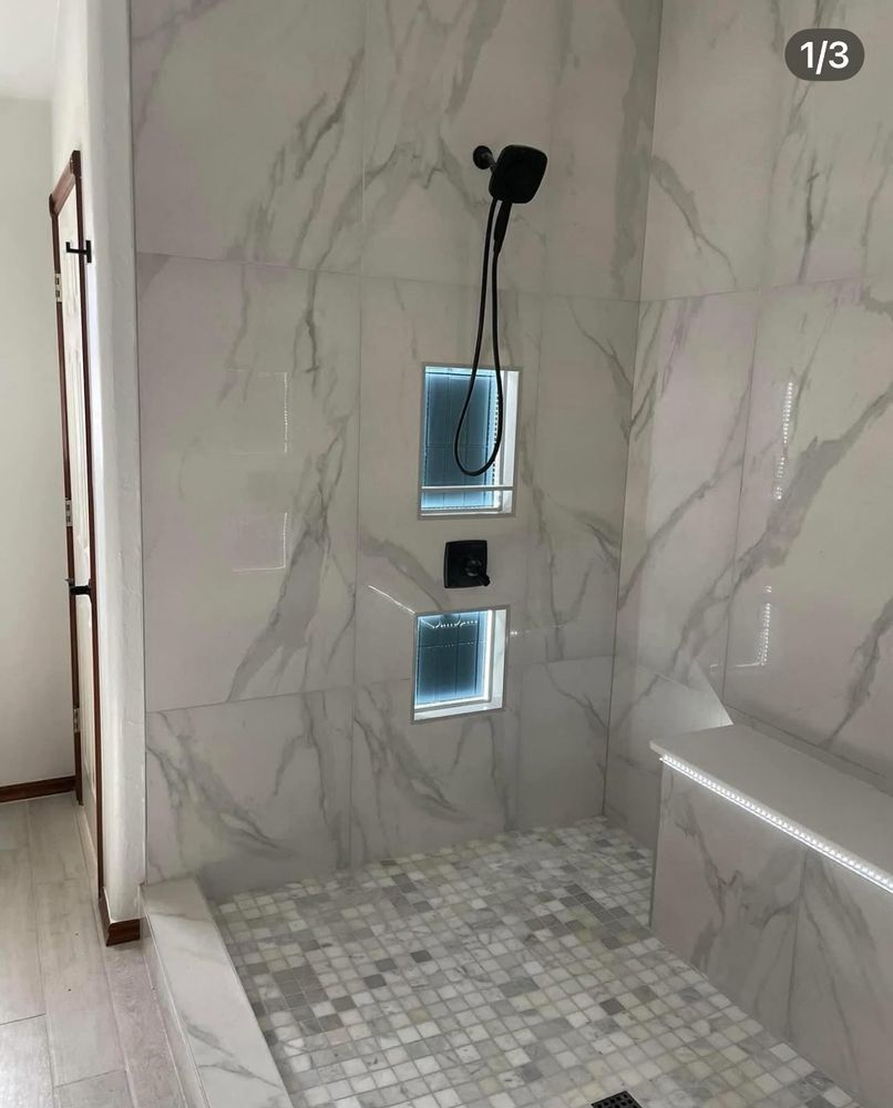 Modern tiled shower with marble-look walls, mosaic floor, and built-in niches with a showerhead above.