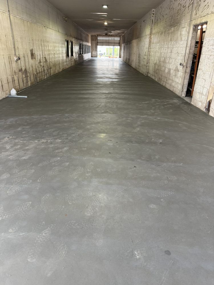 Empty concrete corridor with fresh gray floor and stone walls, lit by daylight at the far end