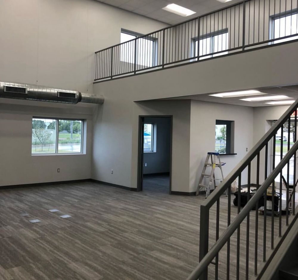 Empty modern office interior with carpeted floor, staircase railing, mezzanine, and large windows