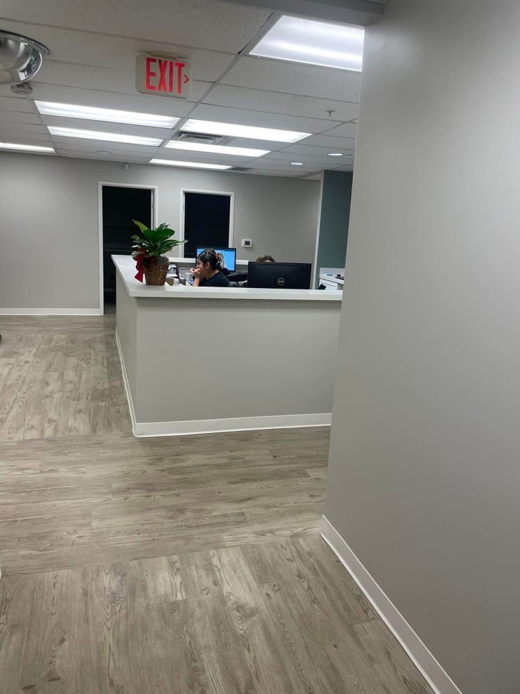 Office lobby with a reception desk, gray walls, white ceiling tiles, and a red exit sign.