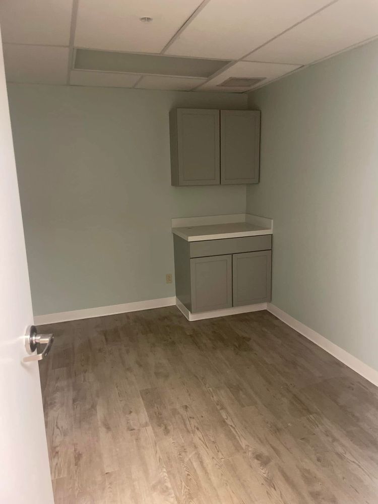 Empty small room with gray walls, wood-look floor, and built-in cabinet/sink area on the far wall