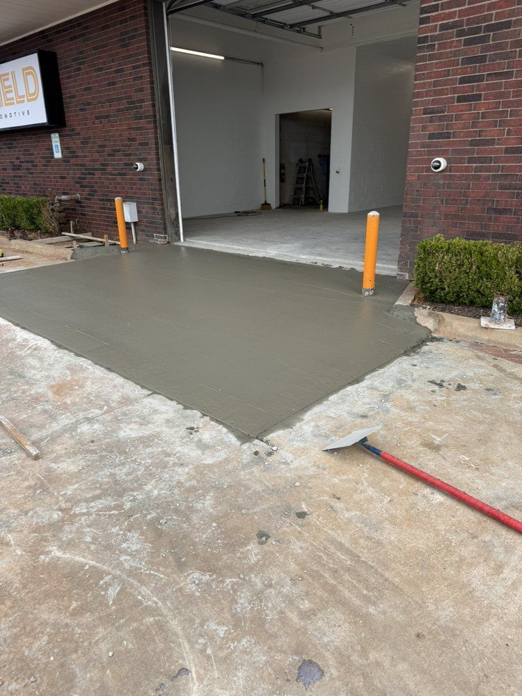 Fresh concrete ramp leading into a garage-style doorway beside a brick building, with orange bollards.