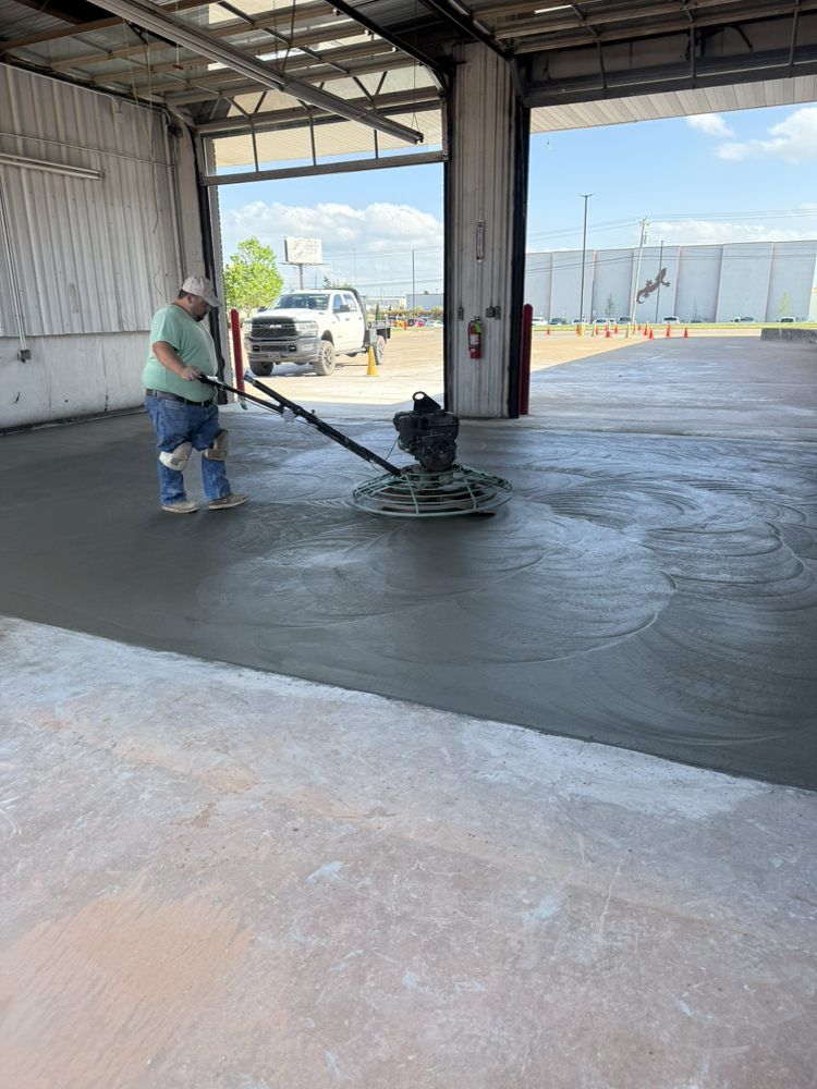 Worker smoothing wet concrete inside a warehouse with a power trowel