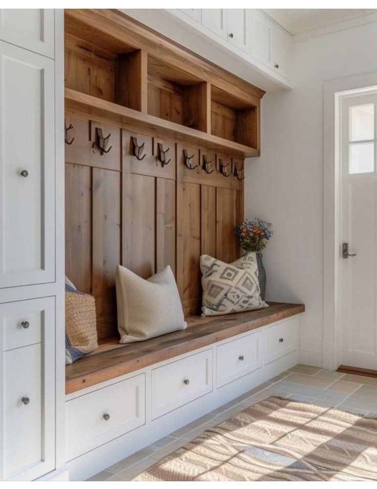 Built-in white mudroom bench with wood hooks, shelves, and pillows in a bright entryway