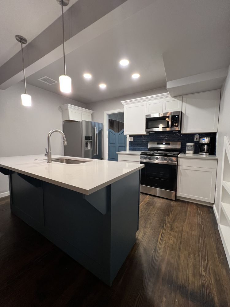 Modern kitchen with white countertops, dark island, stainless appliances, and wood-look flooring