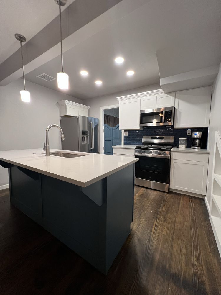 Modern kitchen with white island, stainless appliances, dark wood floor, and pendant lights