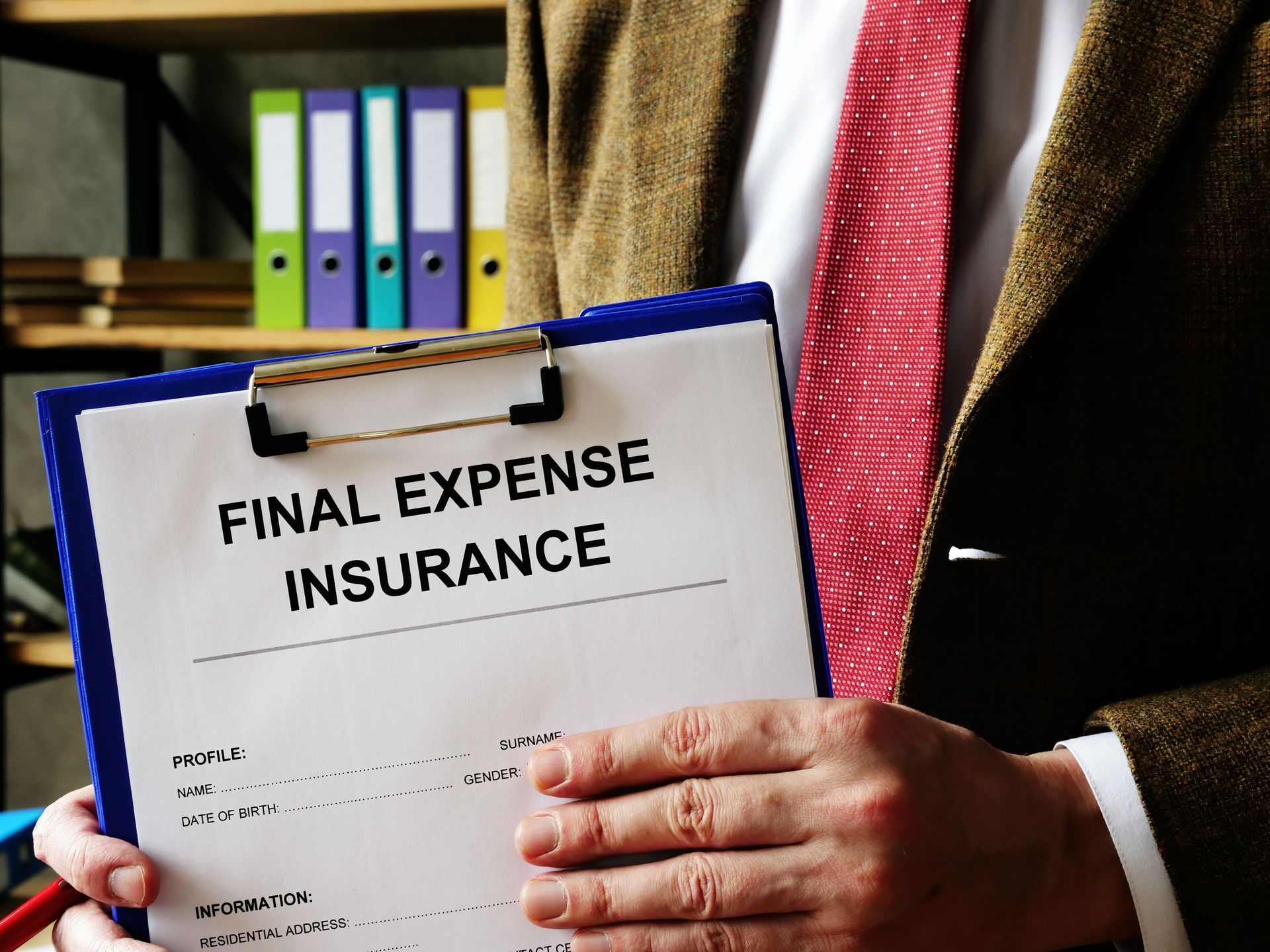 Person holding a clipboard labeled “Final Expense Insurance” in an office setting