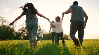 Family holding hands and running through a sunlit grassy field at sunset
