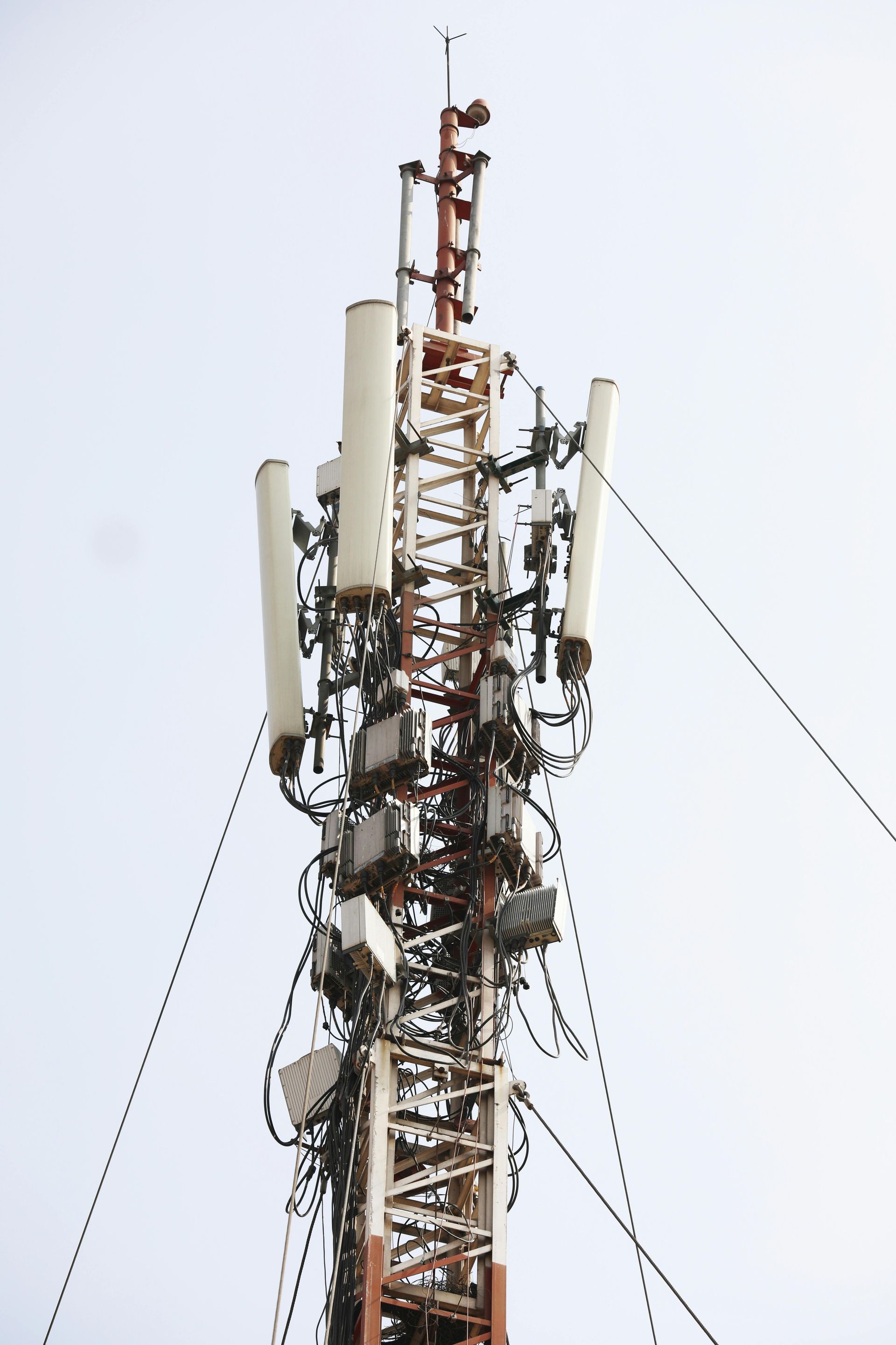 Weathered red-and-white cell tower laden with antennas, rusted gear, and frayed cables