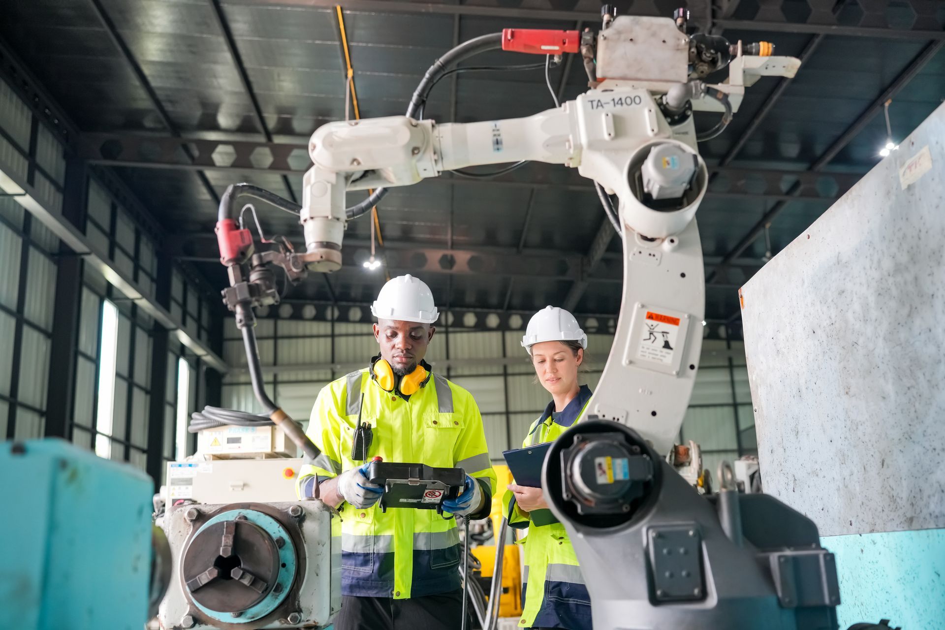 A man and a woman are working on a robotic arm in a factory.