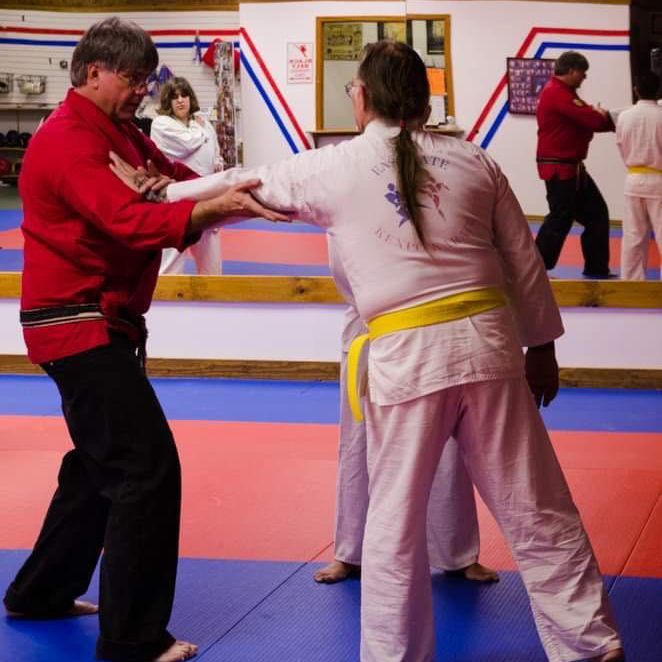 A man in a red shirt is teaching a woman in a white karate uniform