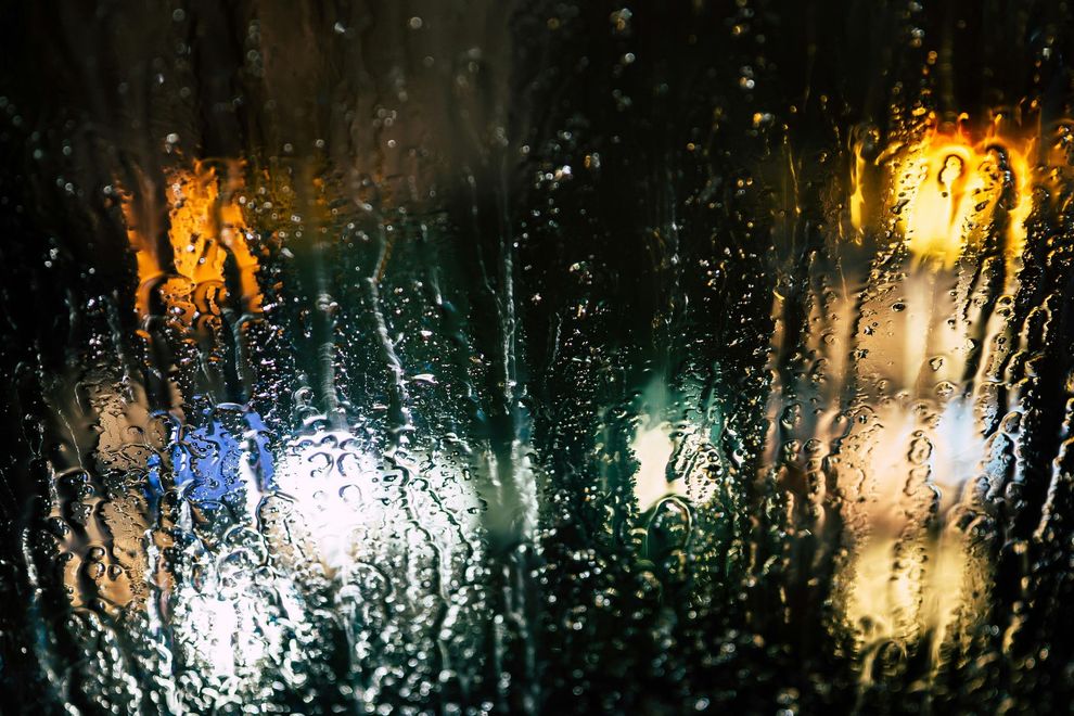 water dripping down a windshield with lights in the background