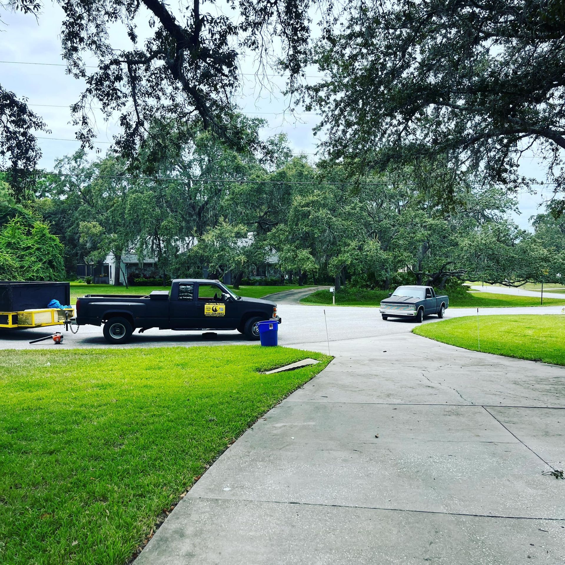 A black pickup truck with a yellow logo parked on a driveway next to a trailer, with another car in the background.