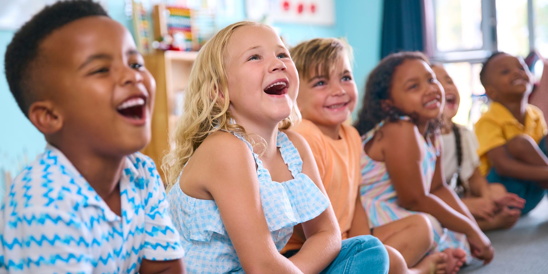 Children sitting in a row, laughing and smiling in a bright classroom