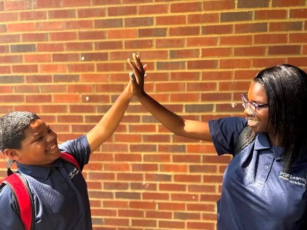 Two people in navy shirts high-five in front of a brick wall.